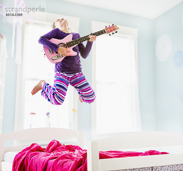 Kaukasisches Mädchen spielt Gitarre auf dem Bett