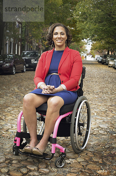 Lächelnde behinderte Frau im Rollstuhl auf einer Kopfsteinpflasterstraße