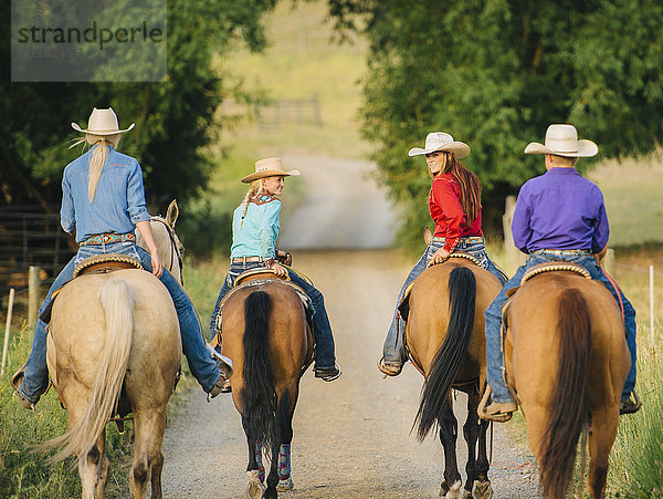 Cowgirls und Cowboy reiten auf Pferden auf einer Landstraße