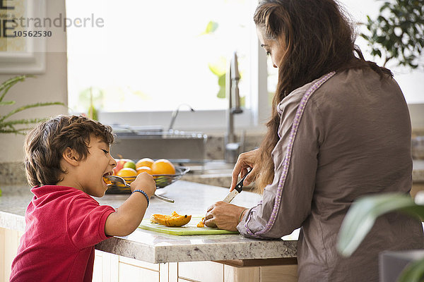 Hispanische Mutter und Sohn essen Obst in der Küche
