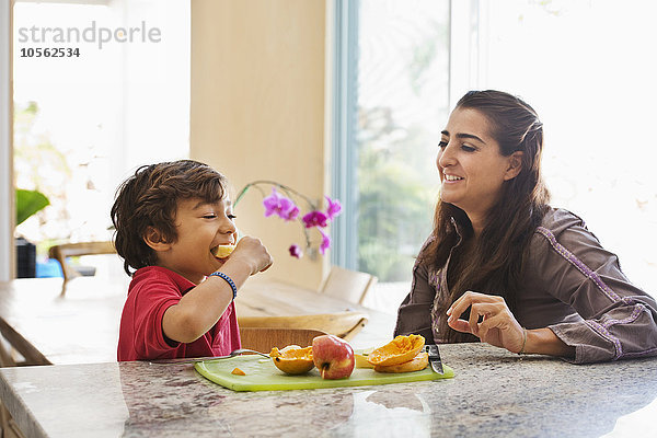 Hispanische Mutter und Sohn essen Obst in der Küche