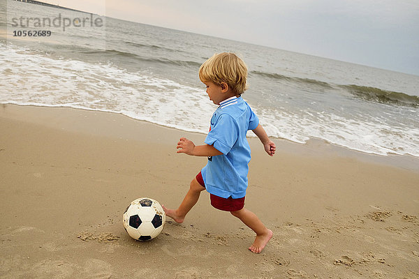 Kaukasischer Junge spielt mit Fußball am Strand