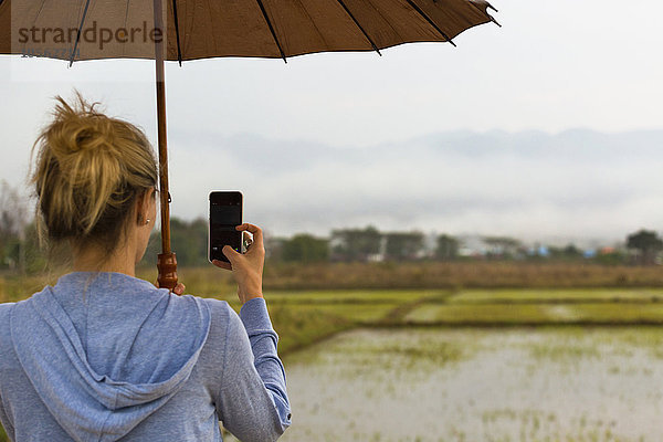 Kaukasische Frau beim Fotografieren ländlicher Reisfelder