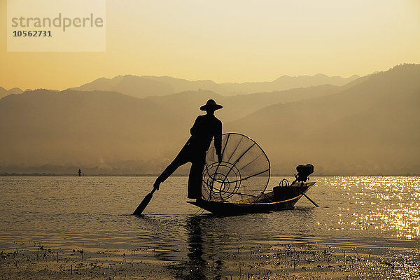 Asiatischer Fischer rudert Kanu auf ländlichem See
