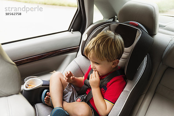 Kaukasischer Junge isst Snack im Autositz