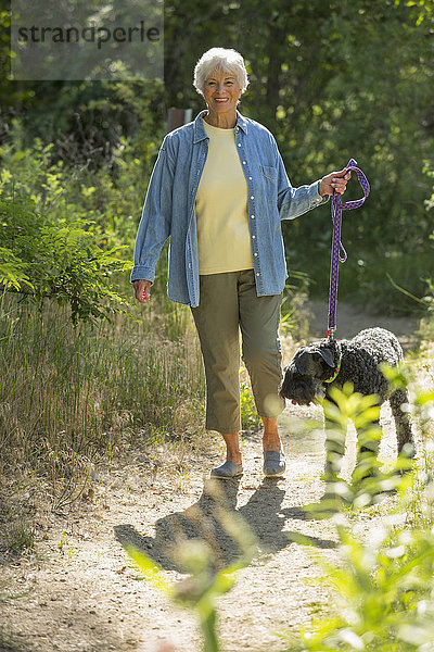 Ältere kaukasische Frau geht mit ihrem Hund auf einem Feldweg spazieren