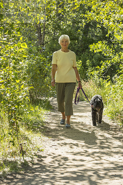 Ältere kaukasische Frau geht mit ihrem Hund auf einem Feldweg spazieren