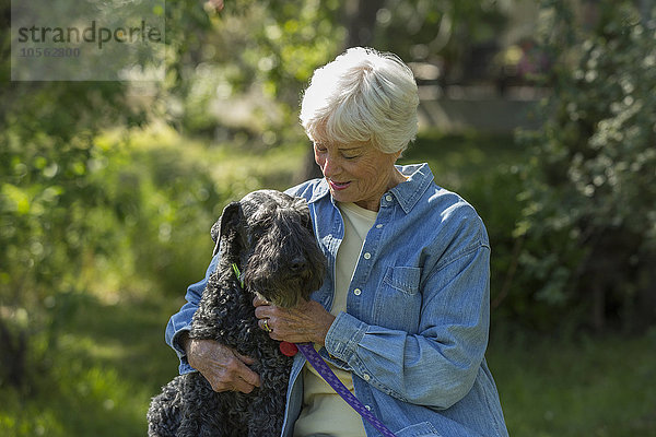 Ältere kaukasische Frau umarmt Hund im Park