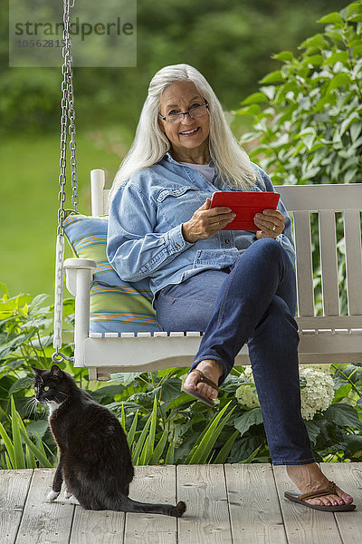 Kaukasische Frau benutzt digitales Tablet auf Veranda-Schaukel