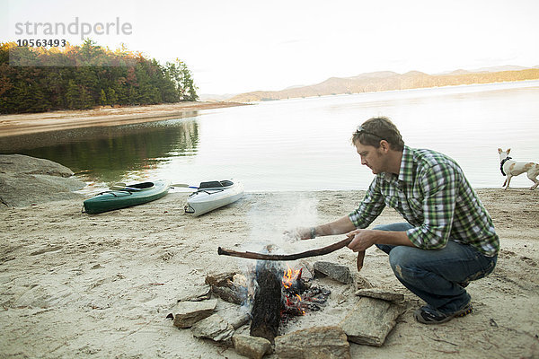 Mann baut Lagerfeuer am See