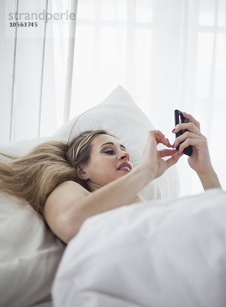 Kaukasische Frau benutzt Mobiltelefon im Bett