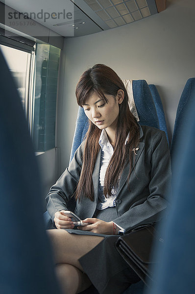 Chinesische Geschäftsfrau benutzt Mobiltelefon im Flugzeug