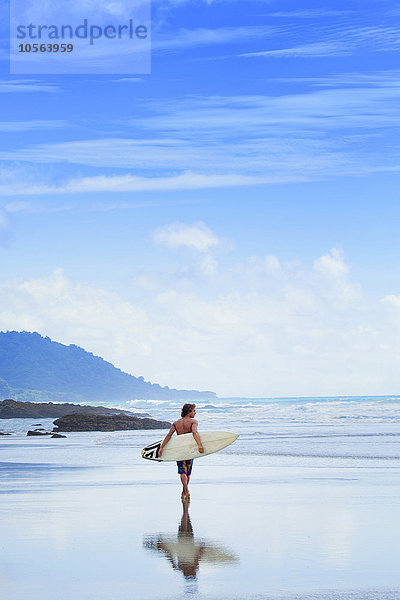 Mann trägt Surfbrett am Strand