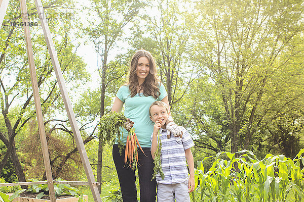 Kaukasische Mutter und Sohn halten Karotten im Garten
