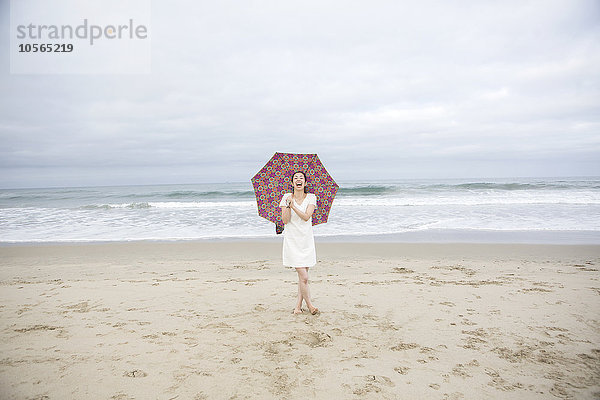 Frau lachend mit Regenschirm am Strand