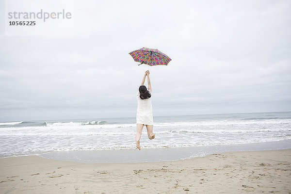 Frau spielt mit Regenschirm am Strand