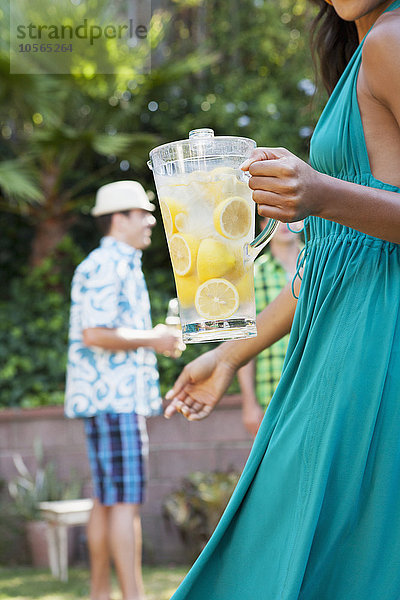 Frau hält Krug mit Limonade beim Grillen im Hinterhof