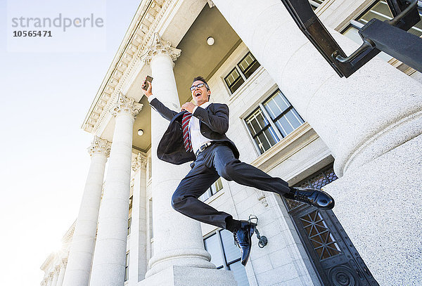 Gemischtrassiger Geschäftsmann springt vor Freude vor dem Gerichtsgebäude herum