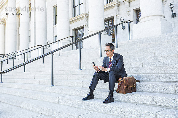 Gemischtrassiger Geschäftsmann benutzt Mobiltelefon auf den Stufen des Gerichtsgebäudes