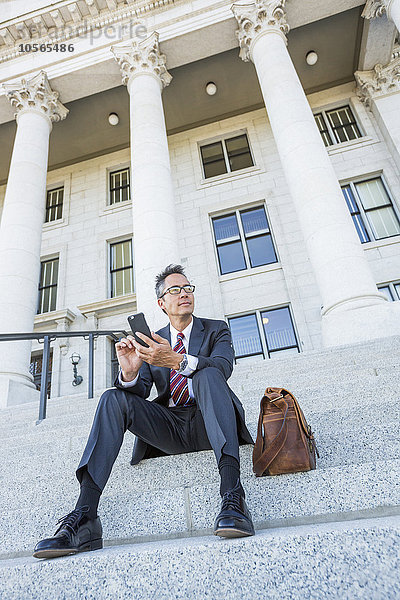 Gemischtrassiger Geschäftsmann benutzt Mobiltelefon auf den Stufen des Gerichtsgebäudes