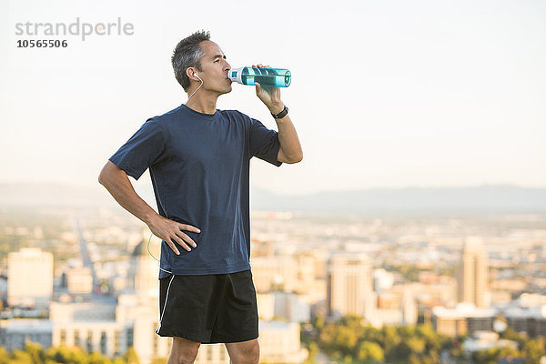Gemischtrassiger Mann trinkt Wasserflasche auf städtischer Anhöhe