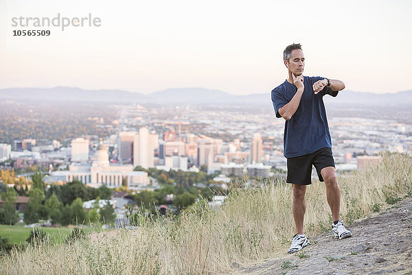 Gemischtrassiger Mann prüft den Puls auf einem Hügel über Salt Lake City  Utah  Vereinigte Staaten