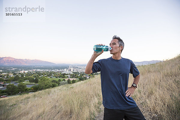 Gemischtrassiger Mann trinkt eine Wasserflasche auf einer Bergkuppe
