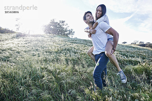 Mann trägt Freundin huckepack auf einem Feld
