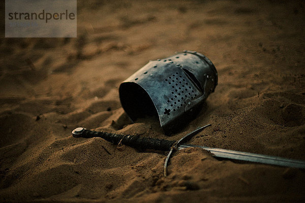 Mittelalterlicher Helm und Schwert im Sand