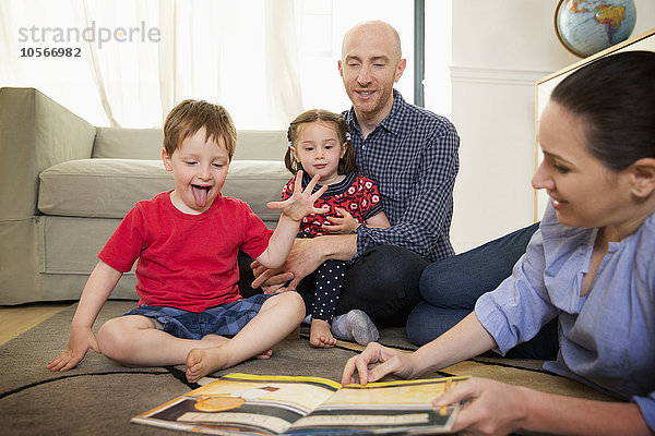 Familie liest Buch auf dem Boden im Wohnzimmer