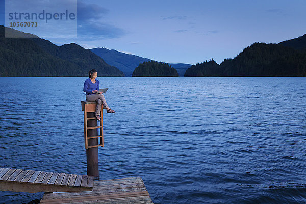 Japanische Frau sitzt auf einem Holzsteg am See