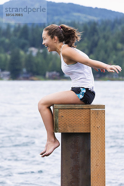 Gemischtrassiges Mädchen sitzt auf einem Holzpodest am See