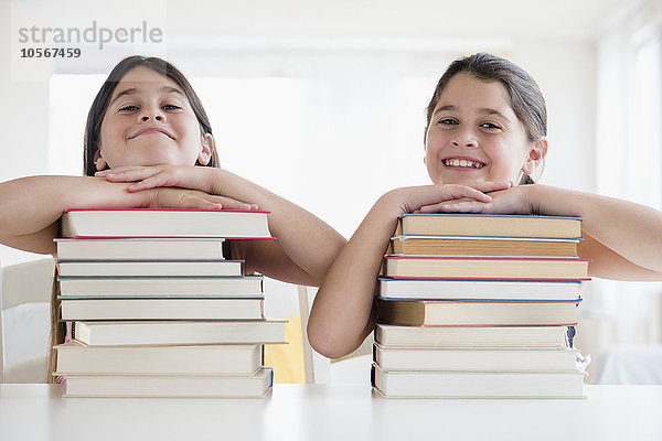 Kaukasische Zwillingsschwestern auf Bücherstapeln ruhend