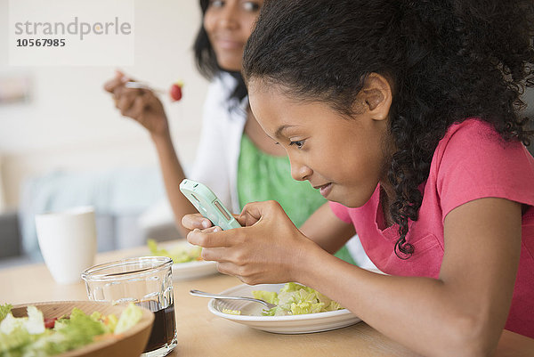 Mädchen benutzt Mobiltelefon beim Abendessen