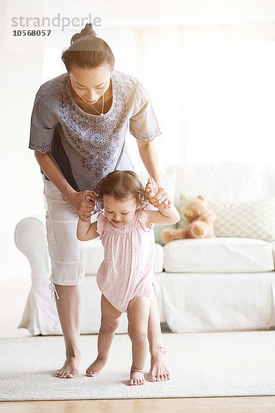 Mutter hilft ihrer kleinen Tochter beim Gehen im Wohnzimmer