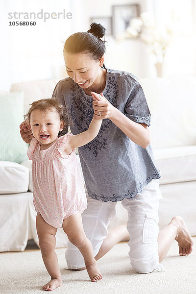 Mutter hilft ihrer kleinen Tochter beim Gehen im Wohnzimmer