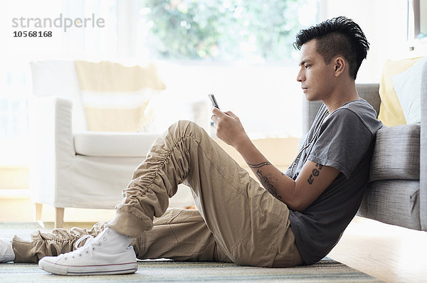 Asiatischer Mann benutzt Mobiltelefon im Wohnzimmer