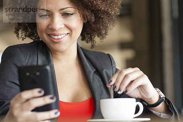 Gemischtrassige Frau benutzt Mobiltelefon in einem Café