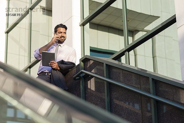 Indischer Geschäftsmann  der auf einer Treppe mit seinem Handy telefoniert