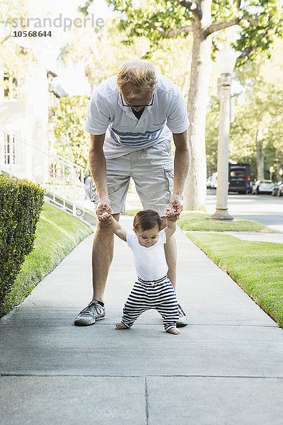 Vater hilft seinem kleinen Sohn beim Gehen auf dem Bürgersteig