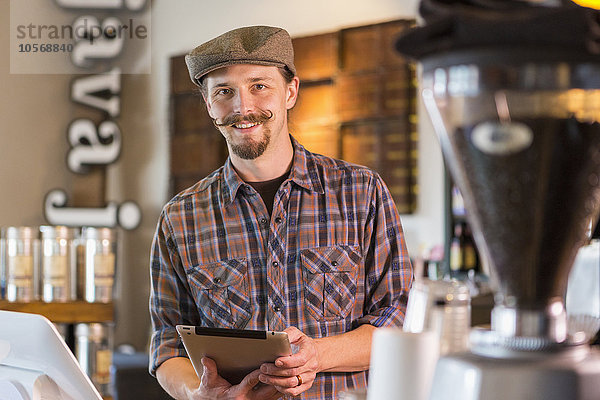 Kaukasischer Barista hält digitales Tablet in einem Café