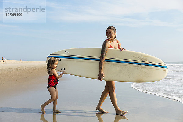 Mutter und Tochter tragen Surfbrett am Strand