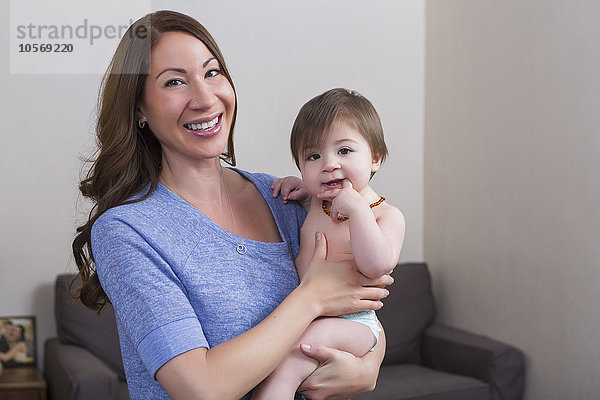 Gemischtrassige Mutter hält ihre kleine Tochter im Wohnzimmer