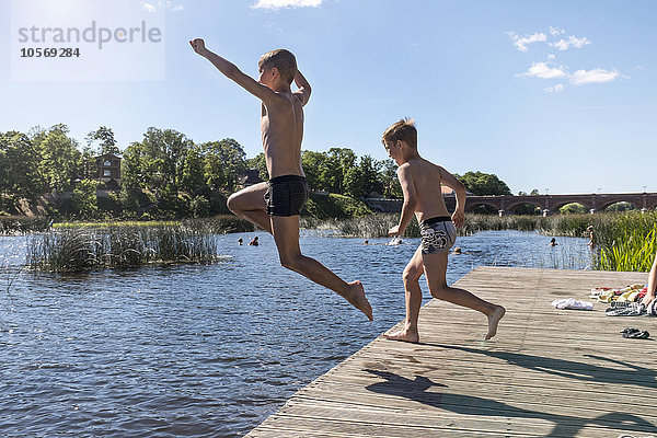 Kaukasische Kinder springen in den See