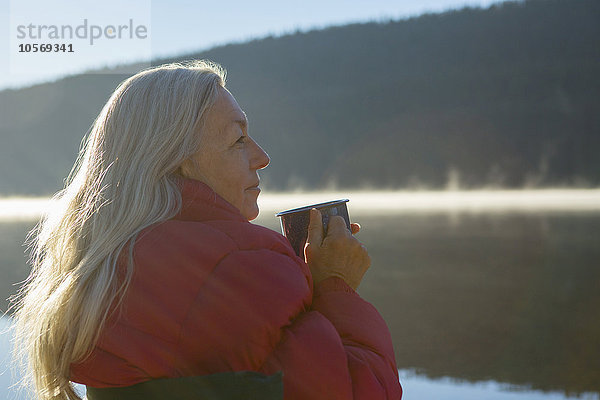 Kaukasische Frau trinkt Kaffee am See