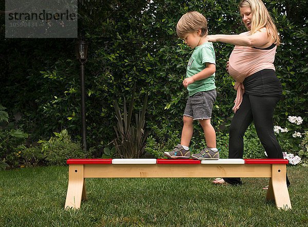 Mutter  die dem Sohn hilft  über die Balancierstange im Garten zu laufen.