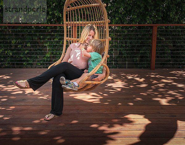 Schwangere Frau und Sohn  entspannen im Gartenschaukelstuhl