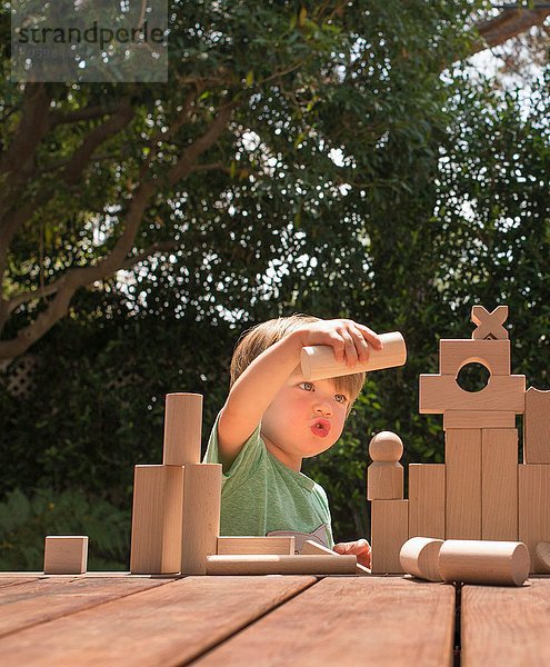 Junge spielt mit Holzbausteinen im Garten