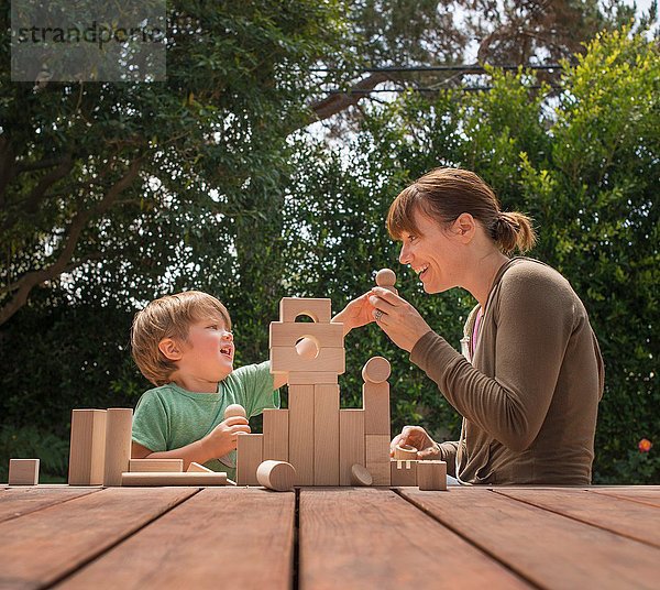 Mutter und Sohn spielen mit Holzbausteinen im Garten