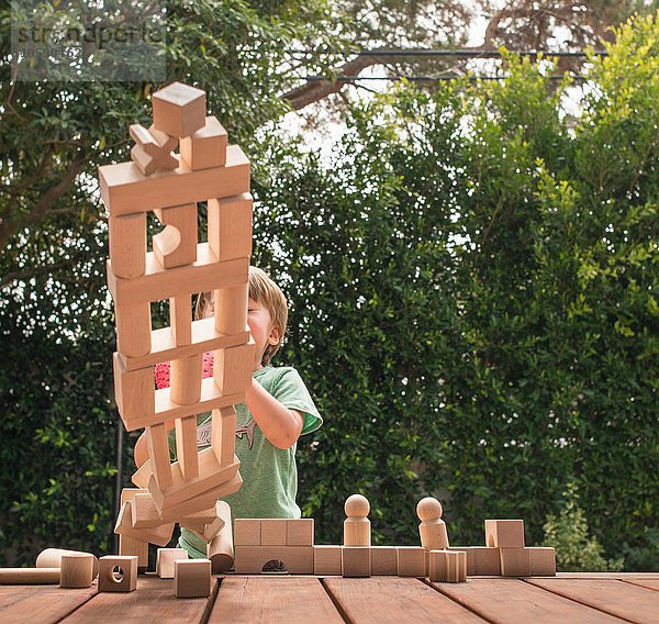 Junge schiebt über Holzkonstruktion aus Bauklötzen  im Freien